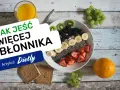 Jak jeść więcej błonnika? Miska pełna owoców, nasion chia i jagód, obok pieczywo pełnoziarniste i sok.