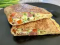 Keto tortilla przepis: złocisty placek z jajek, szynki, pomidorów i szczypiorku, złożony na pół, na czarnym talerzu.