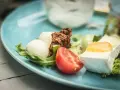 Pyszne keto śniadanie: ser brie z dżemem, kulki mozzarelli, pomidor i rukola na błękitnym talerzu.