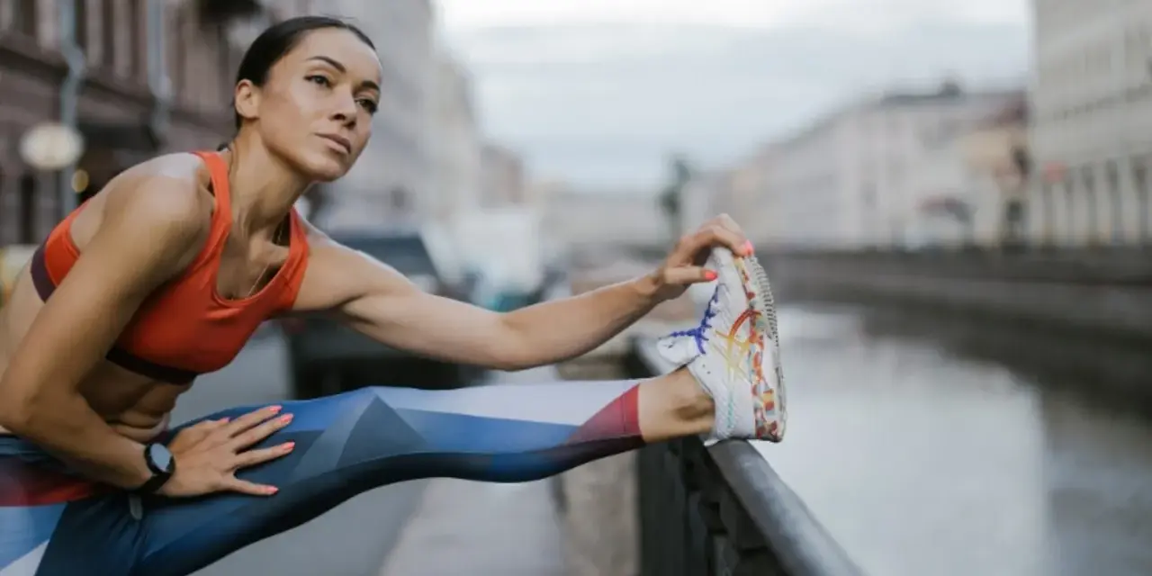 Kobieta w sportowym stroju rozciąga nogę, przygotowując się do treningu cardio nad kanałem.