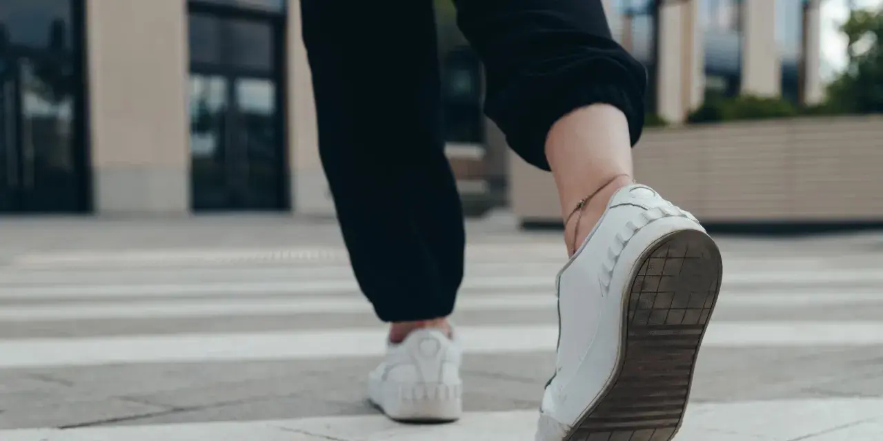 Kobieta w białych sneakersach idzie po pasach, licząc ile kroków dziennie.