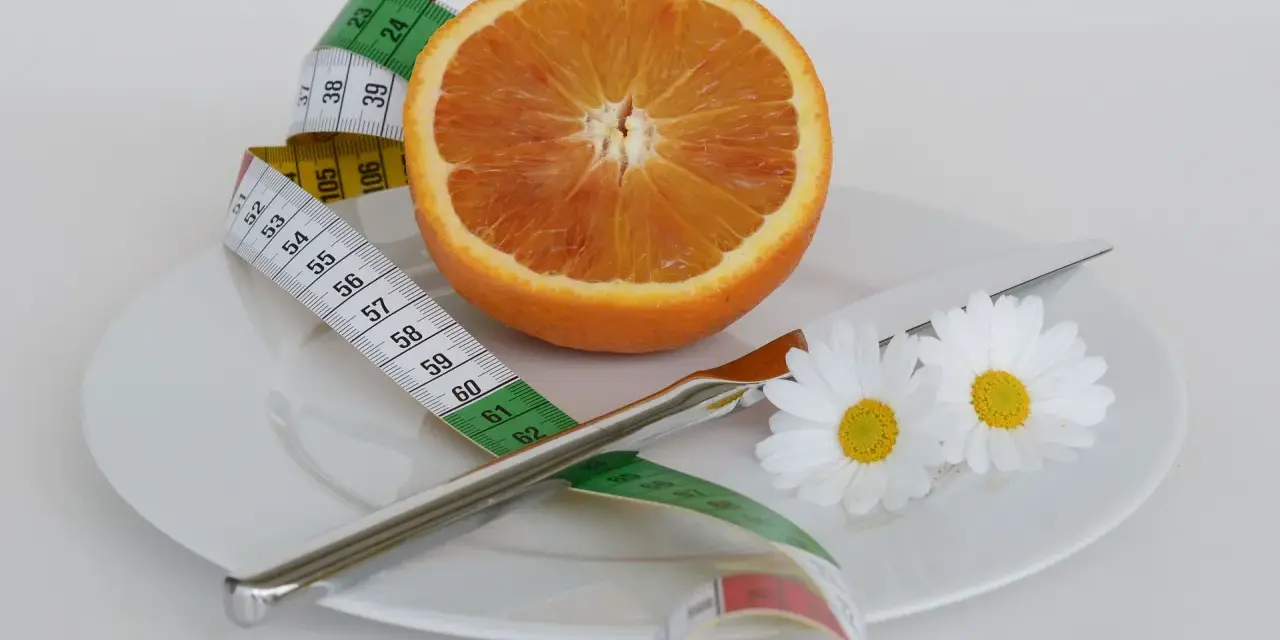 Pomarańcza na talerzu z miarką krawiecką i kwiatami symbolizuje zdrową dietę odchudzającą.