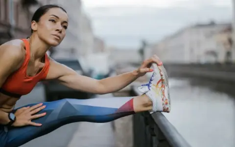 Kobieta w sportowym stroju rozciąga nogę, przygotowując się do treningu cardio nad kanałem.