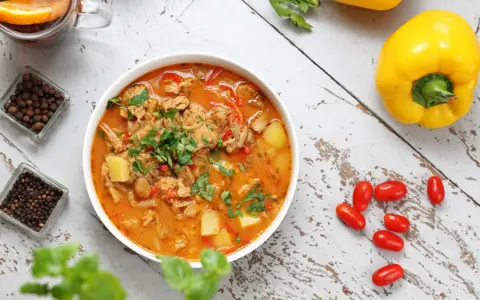 Gulasz warzywny z ziemniakami i papryką, idealny na dietę trzustkową. Obok kubek herbaty z pomarańczą i przyprawy.