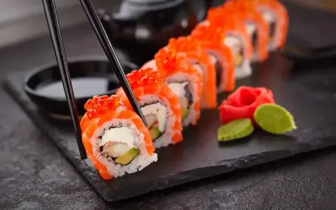 Chopsticks podnoszą kawałek sushi z łososiem i ikrą. Czy sushi jest lekkostrawne? Zależy od składników, ale ten wygląda apetycznie.