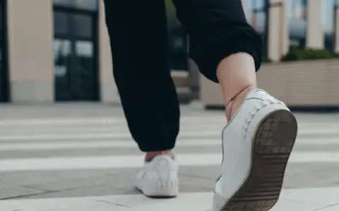 Kobieta w białych sneakersach idzie po pasach, licząc ile kroków dziennie.