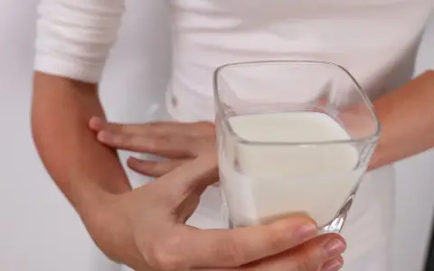 Osoba z zaczerwienionym ramieniem trzyma szklankę mleka, sugerując problem z nietolerancją laktozy.