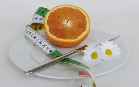 Pomarańcza na talerzu z miarką krawiecką i kwiatami symbolizuje zdrową dietę odchudzającą.