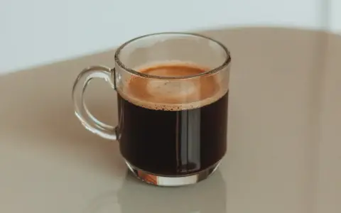 Kawa po kolonoskopii, w szklanej filiżance, z pianką na wierzchu.