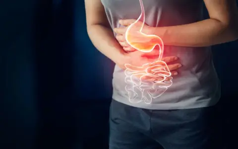 Osoba trzyma się za brzuch, gdzie widoczny jest podświetlony żołądek i jelita, sugerując ból lub problem, jak nadżerka żołądka.