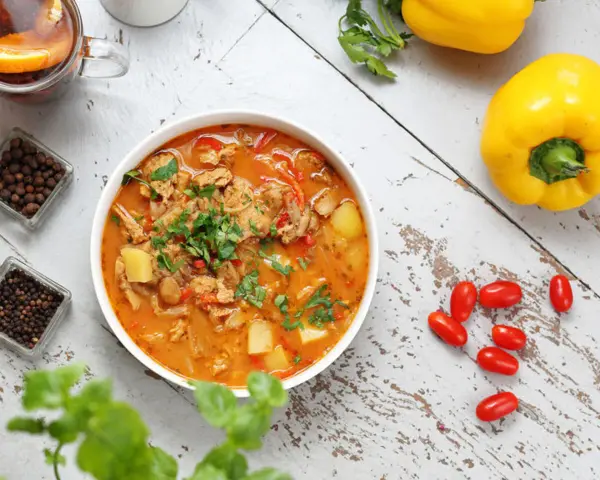 Gulasz warzywny z ziemniakami i papryką, idealny na dietę trzustkową. Obok kubek herbaty z pomarańczą i przyprawy.