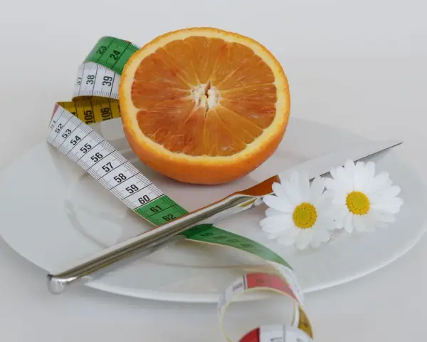 Pomarańcza na talerzu z miarką krawiecką i kwiatami symbolizuje zdrową dietę odchudzającą.