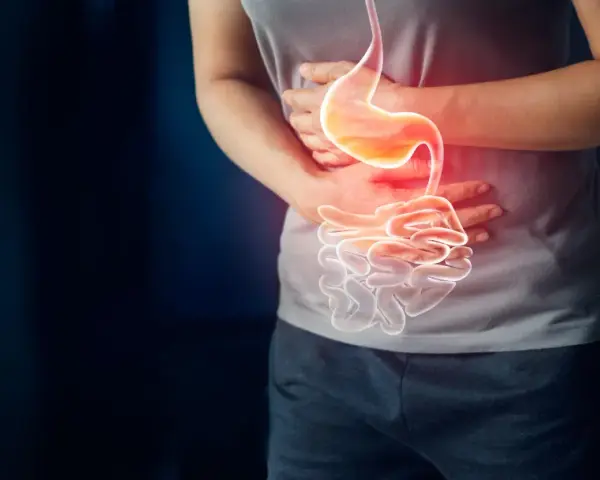 Osoba trzyma się za brzuch, gdzie widoczny jest podświetlony żołądek i jelita, sugerując ból lub problem, jak nadżerka żołądka.