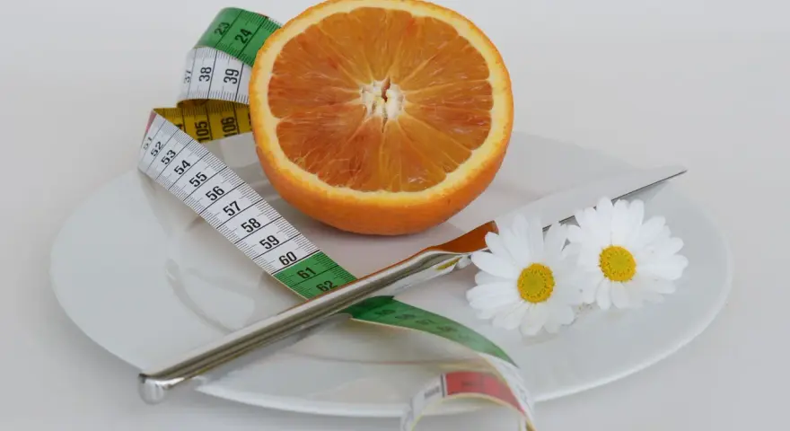 Pomarańcza na talerzu z miarką krawiecką i kwiatami symbolizuje zdrową dietę odchudzającą.